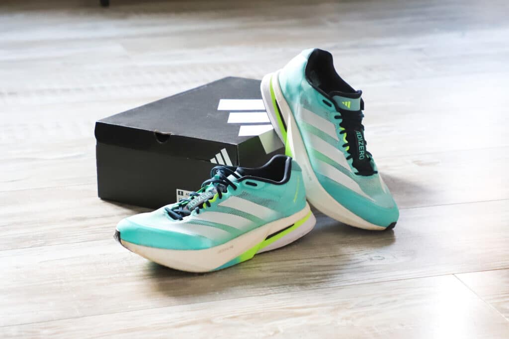 Avis Adidas Boston 13 : Le test sans filtre après 100 km de bitume Présentation des Adidas Boston 13 à côté de leur boîte noire Adidas sur un parquet clair.