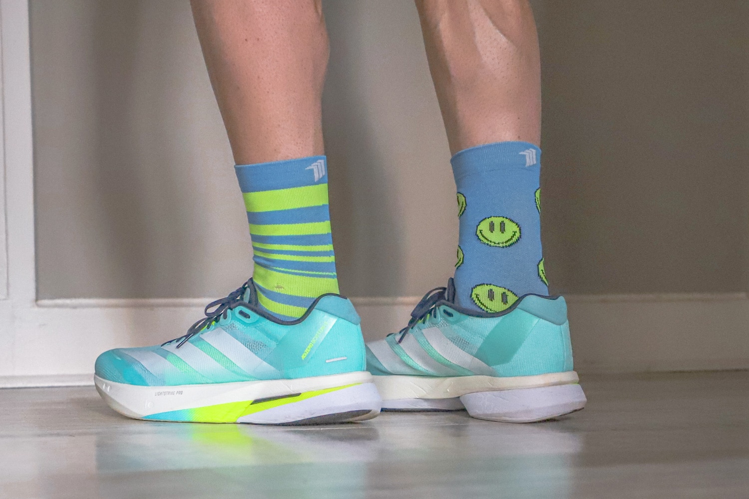 Vue latérale des chaussures Adidas Adizero Boston 13 bleu turquoise portées avec des chaussettes dépareillées (rayures et smileys).